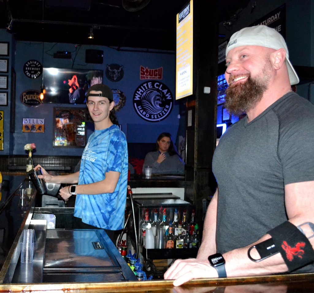 Two people working behind the bar at Corner — one making a drink at the rail, the other leaning on the bar top.