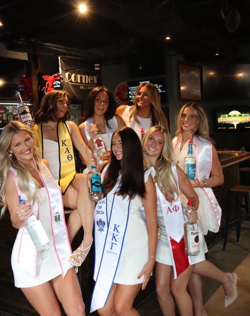 A group gathered at the bar under the lit Corner sign, dressed up and out together for the night.